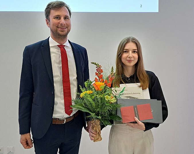 Ein Mann und eine Frau stehen nebeneinander, die Frau hat Blumen und mehrere Gegenstände in der Hand
